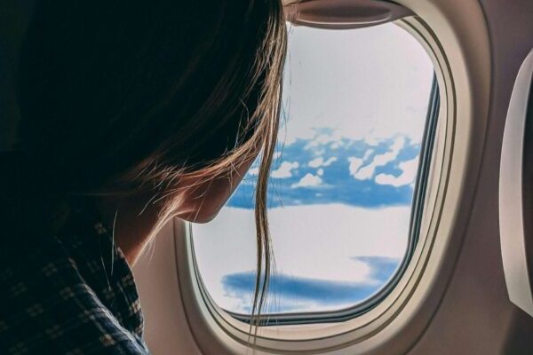 A woman looks out an airplane window, capturing a serene view of clouds and sky during a flight.
